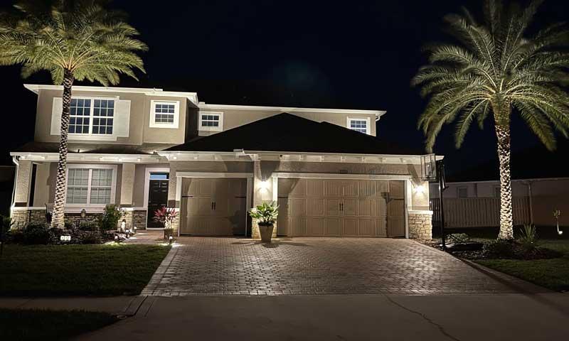 Two-story Florida home at night with uplit palms and driveway lighting
