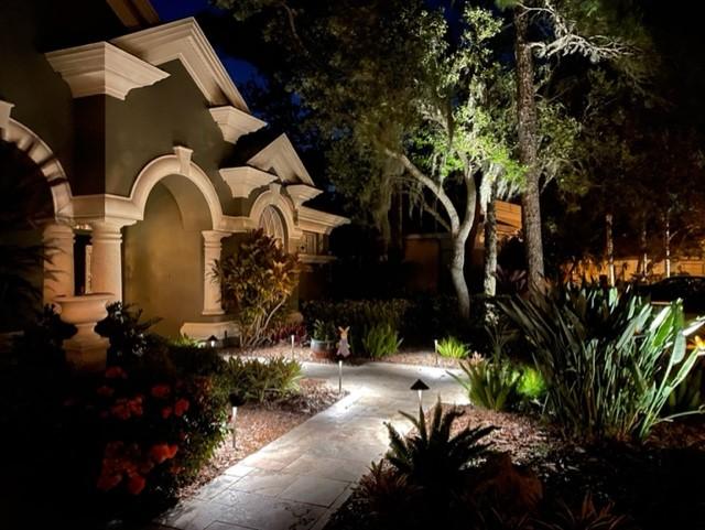 Arched stone entryway with lit walkway and uplit oaks